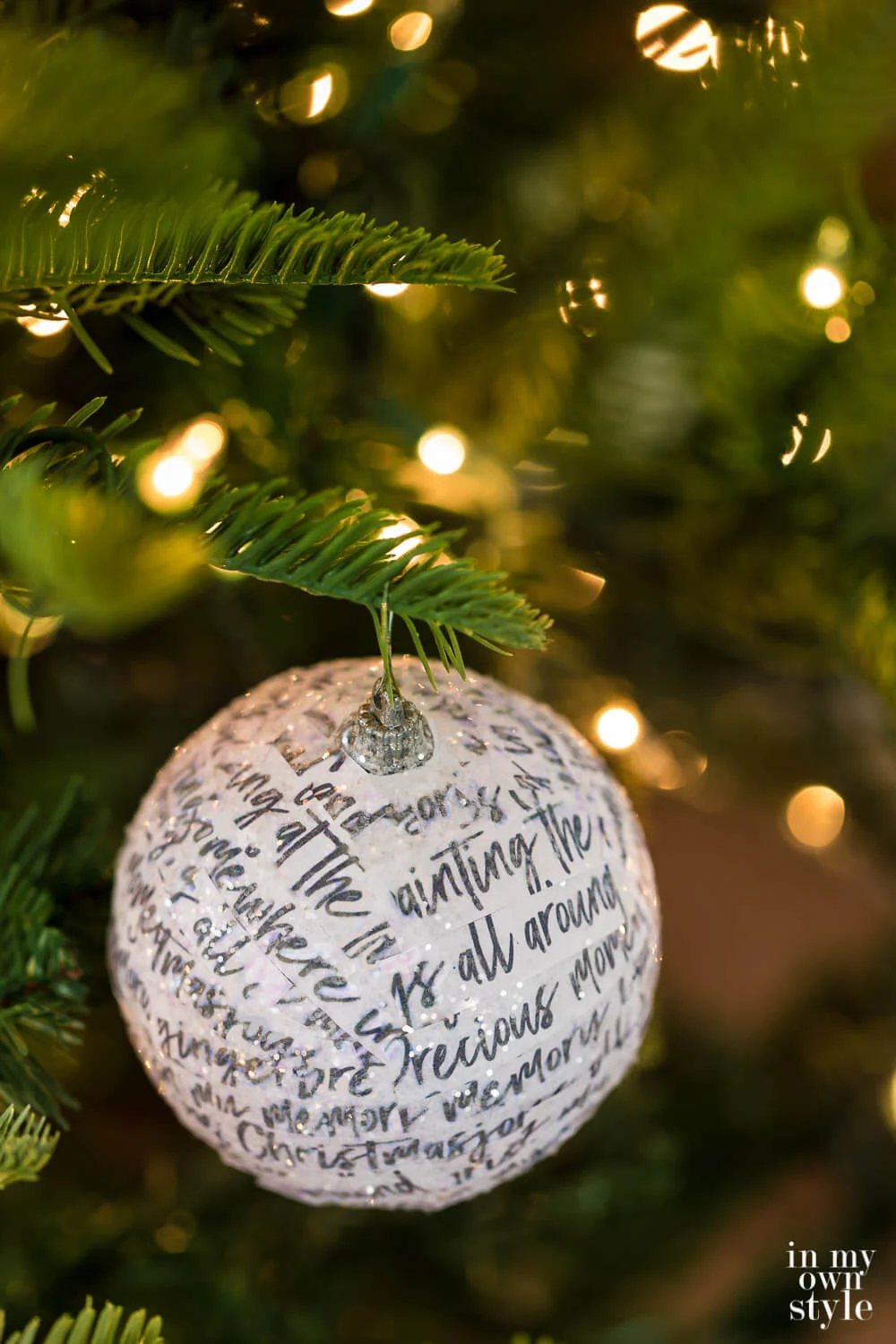 Grey Hand writing white paper strips covering a round ball ornament on a Christmas tree.