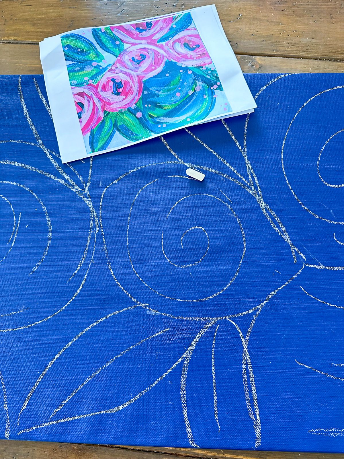sketching blue painted art canvas with white chalk to draw flowers and leaves