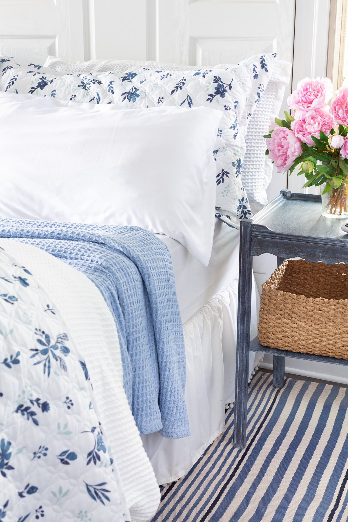 A king size bed made up in a reversible floral bedspread, waffle weave duvet cover and sky blue blanket.
