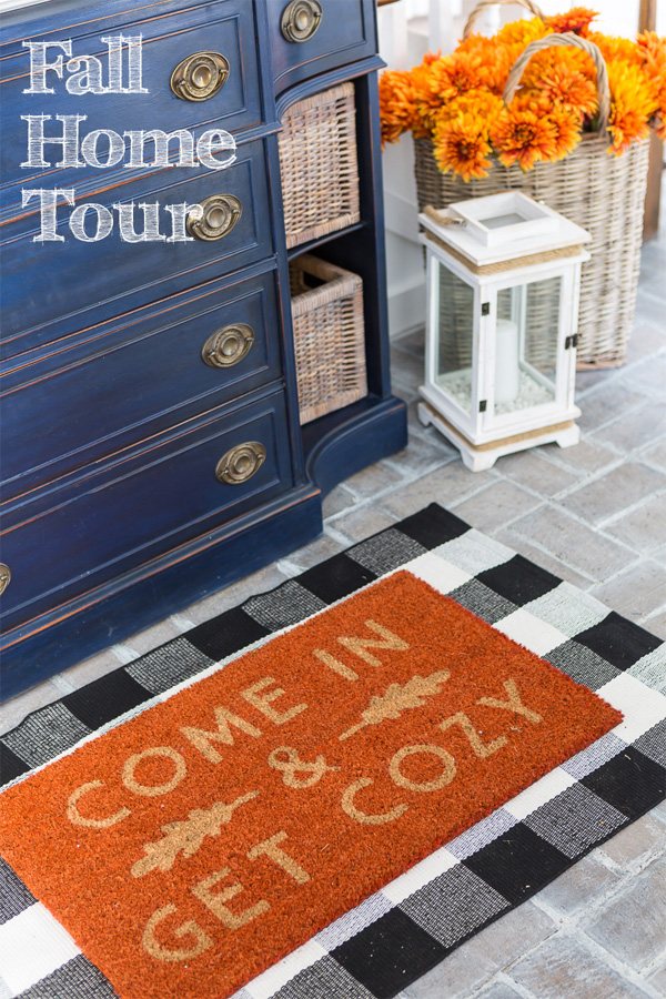 Blue sideboard in a home's entry foyer with fall door mat in front of it that says, come in and get cozy.
