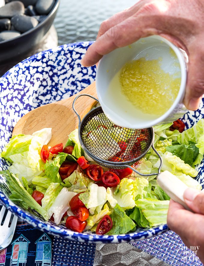 Pouring garlic oil over lettuce to make Caesar Salad.