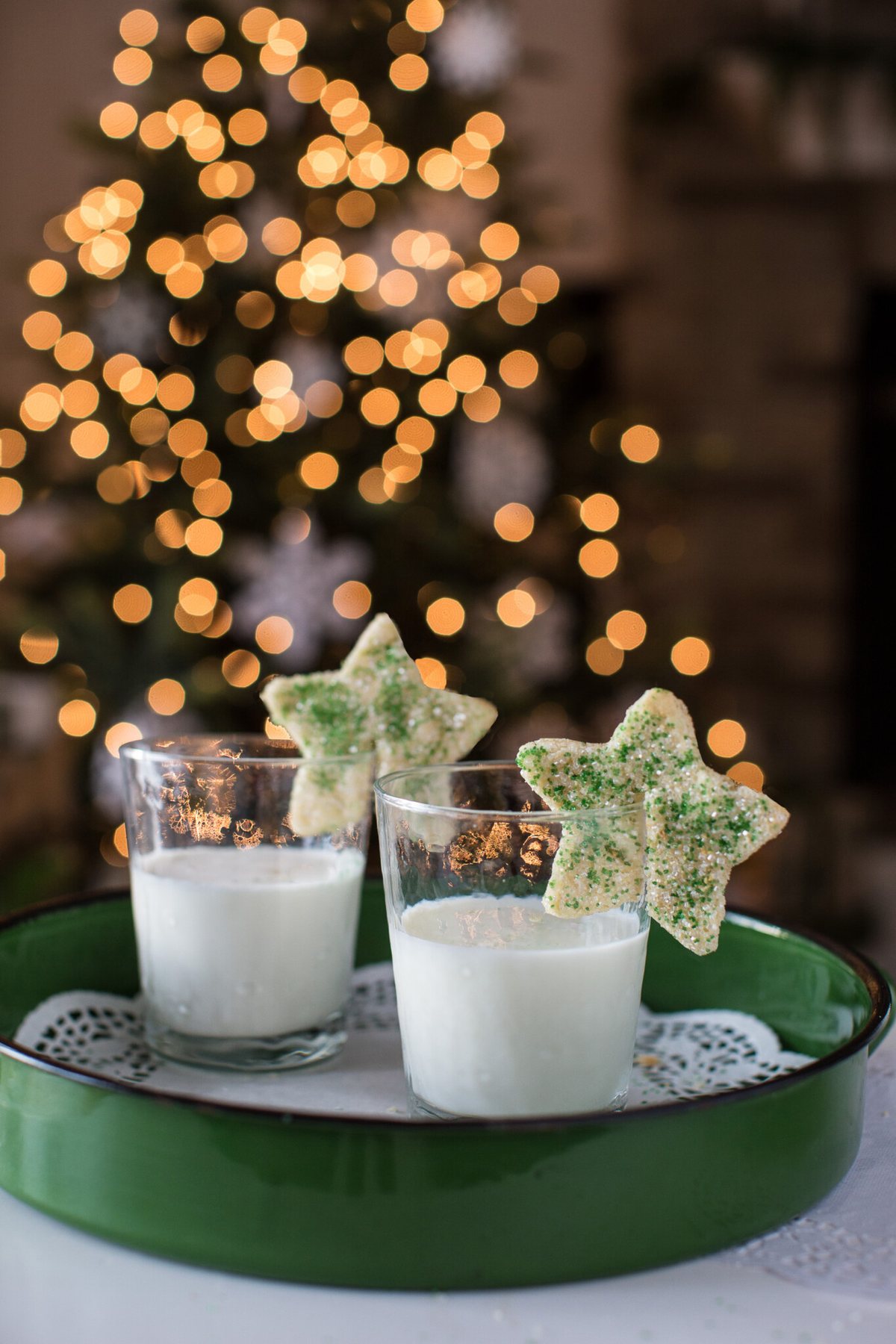 Two star shaped cookies sitting on the rims of milk filled drinking glasses.