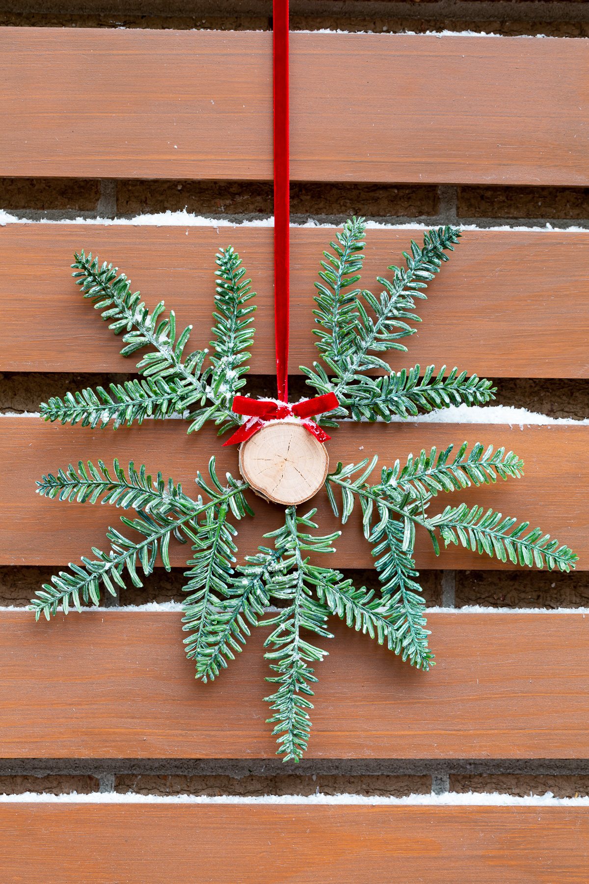 Tree trunk and pine branch Christmas wreath hung on red ribbon outside