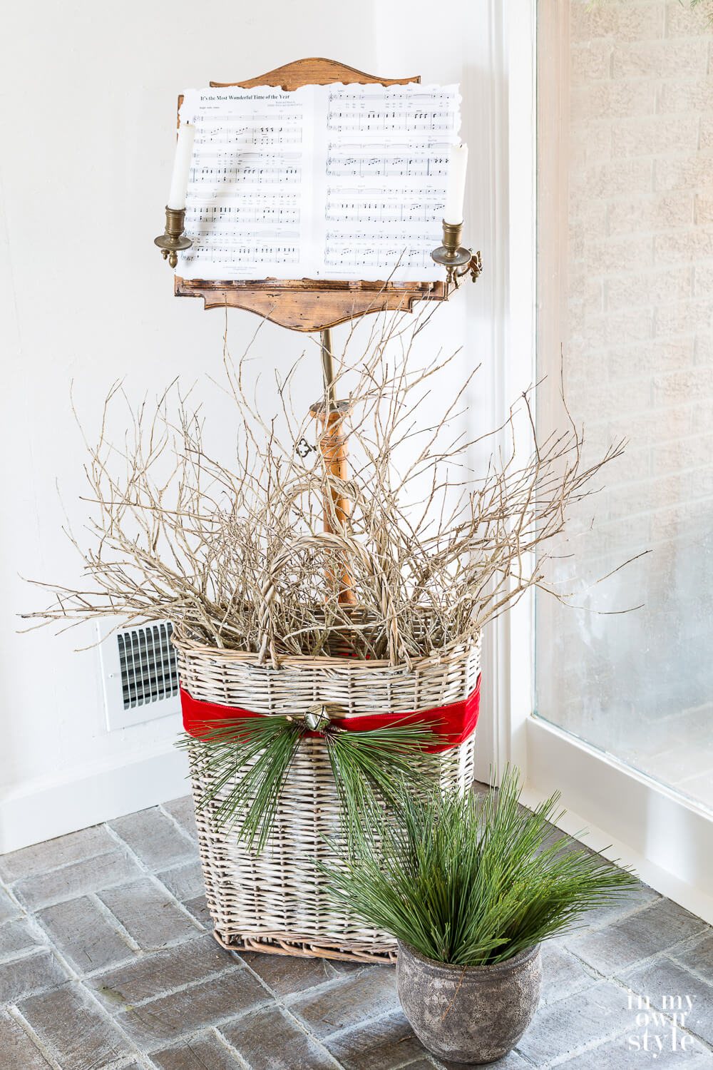 Antique music stand with Christmas music on it. Basket filled with branches in front of it.