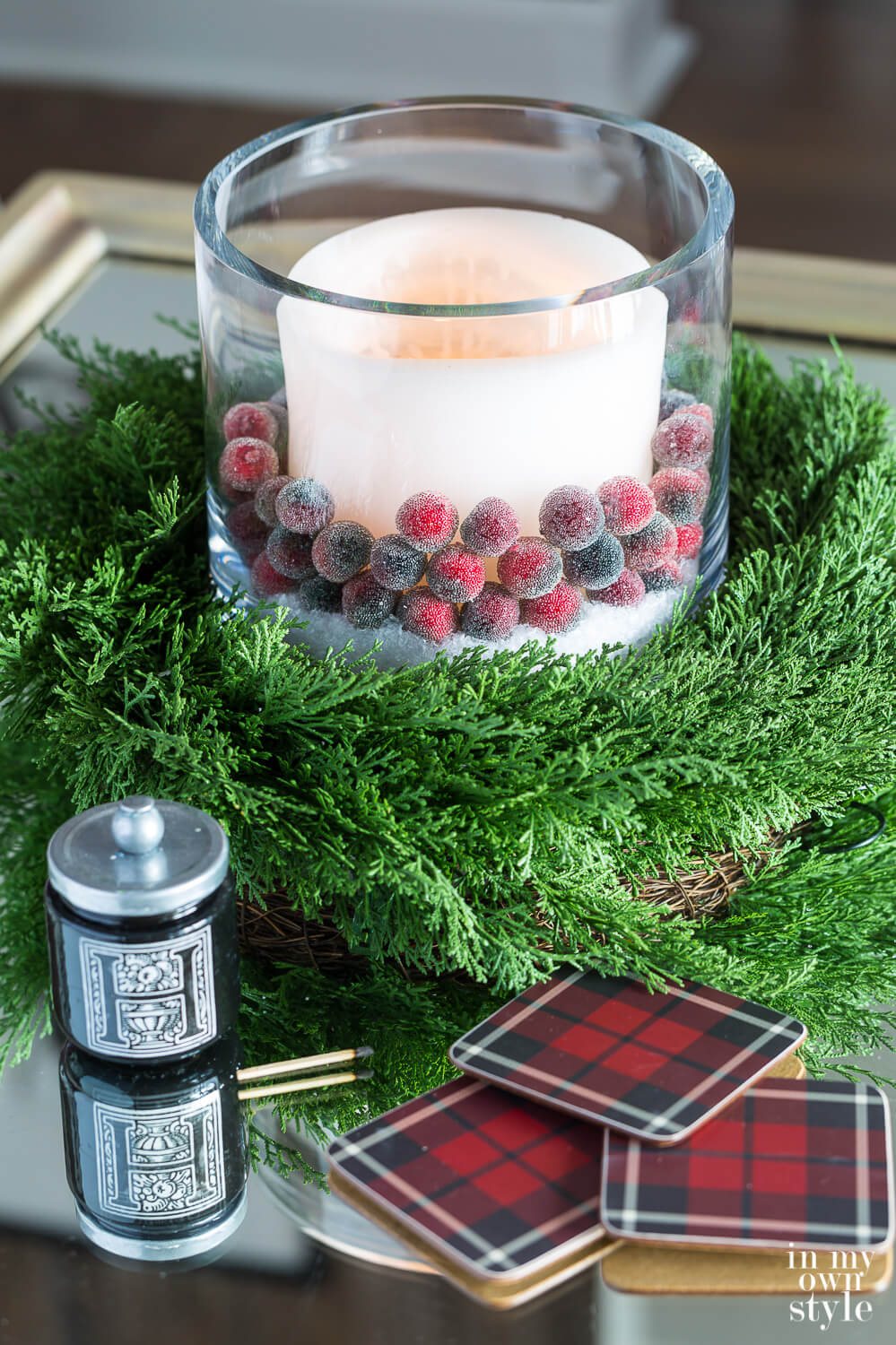 White candle with cranberries around it sitting on a cedar wreath on living room coffee table decorated for Christmas