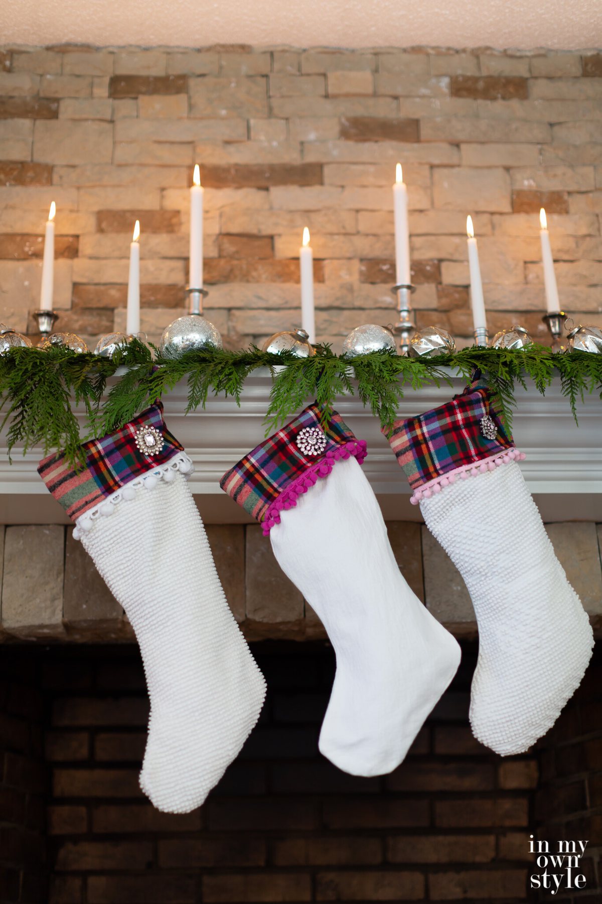 Silver ornaments and candleholders with white candles on a mantel decorated for Christmas