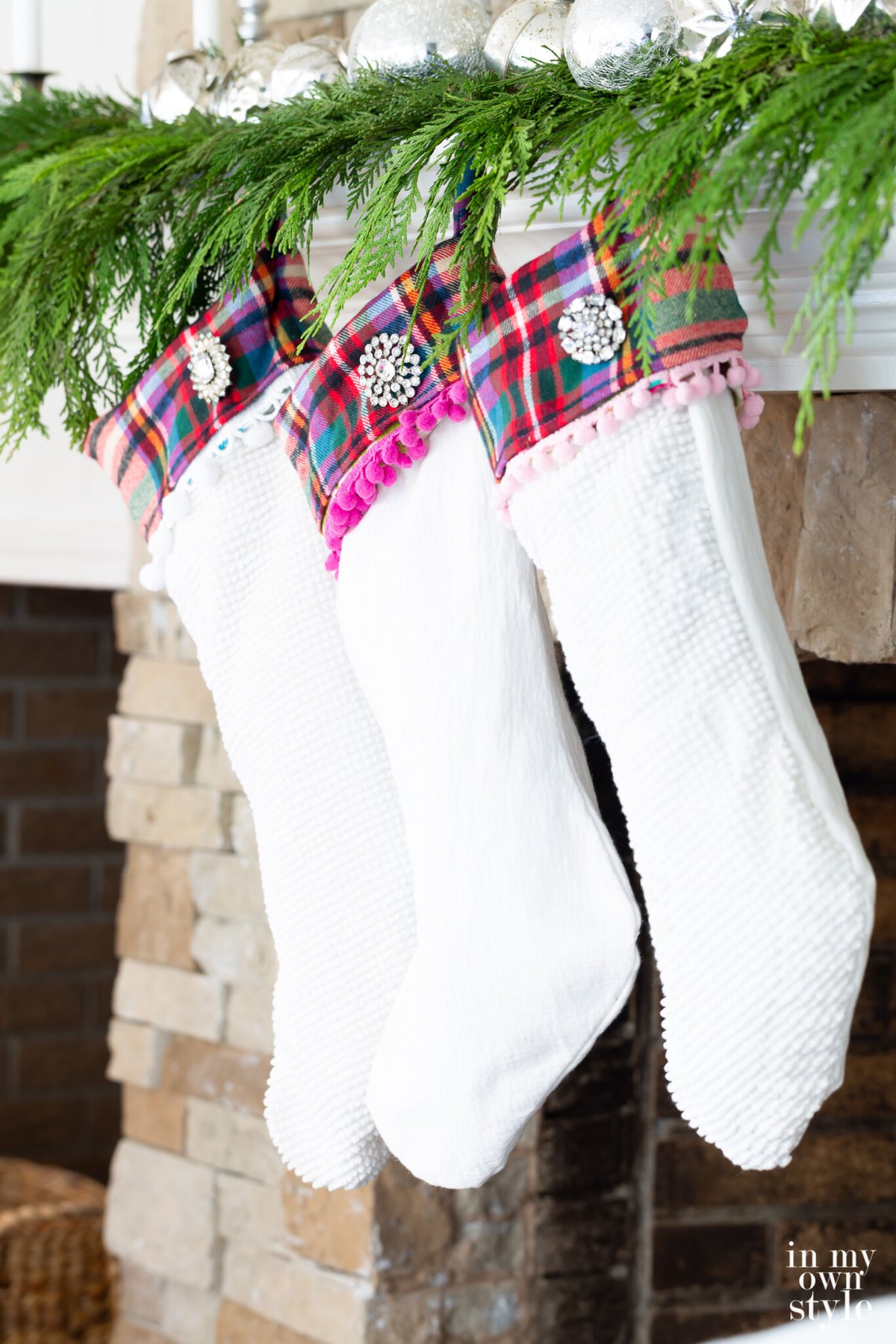 3 White Christmas stockings hanging on cedar draped fireplace mantel