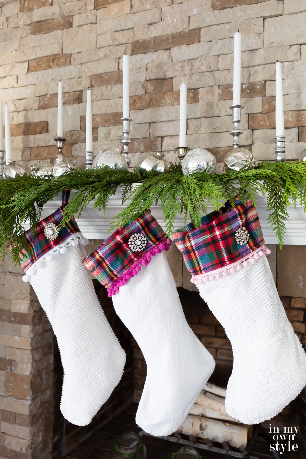 Close up photo of 3 Christmas stockings hanging along cedar trimmed fireplace mantel