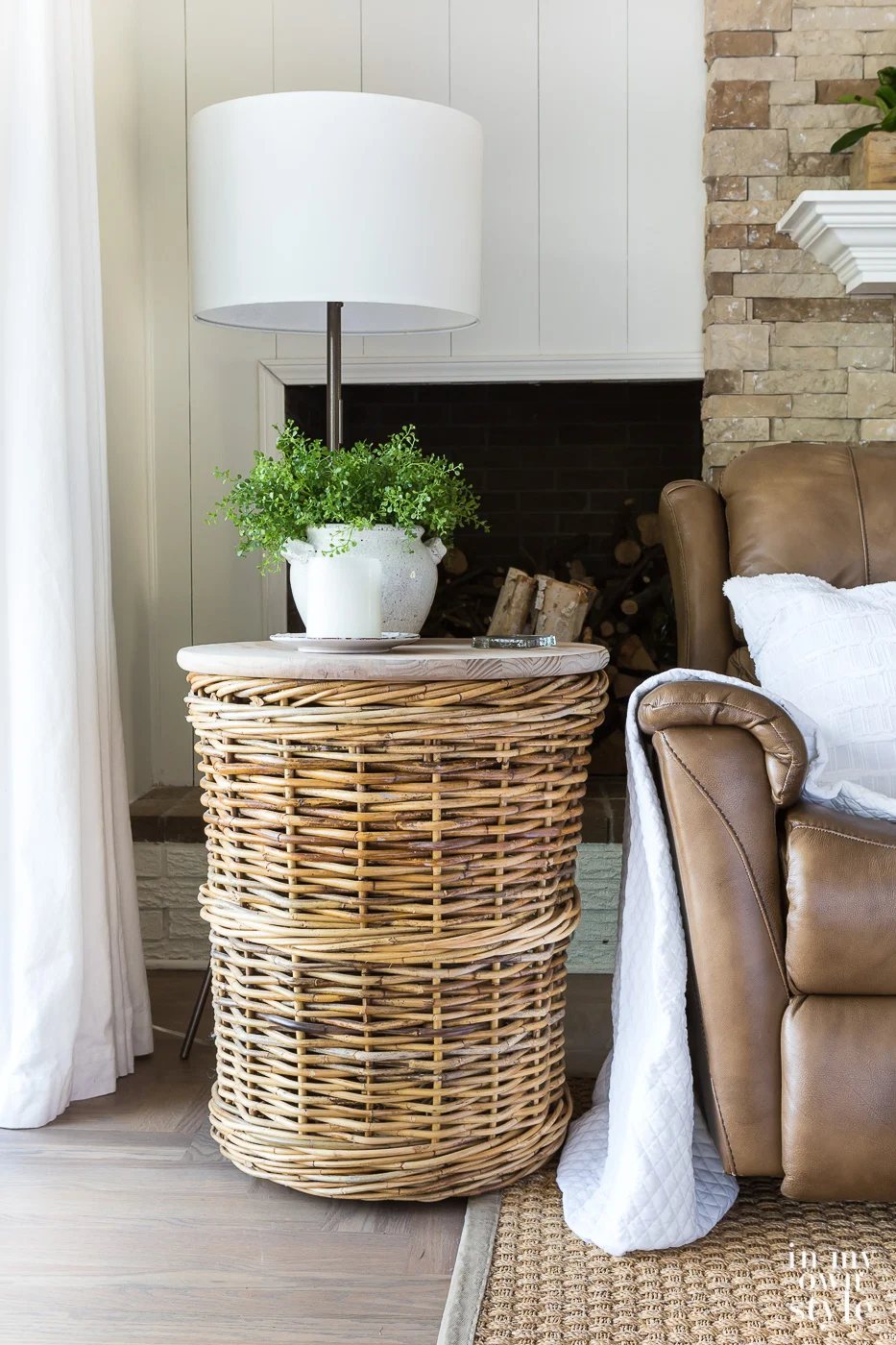 Large basket made into a diy end table. It sits next to a brown leather recliner with a white throw and pillow. A floor lamp behind with a dimmable socket to adjust the light.