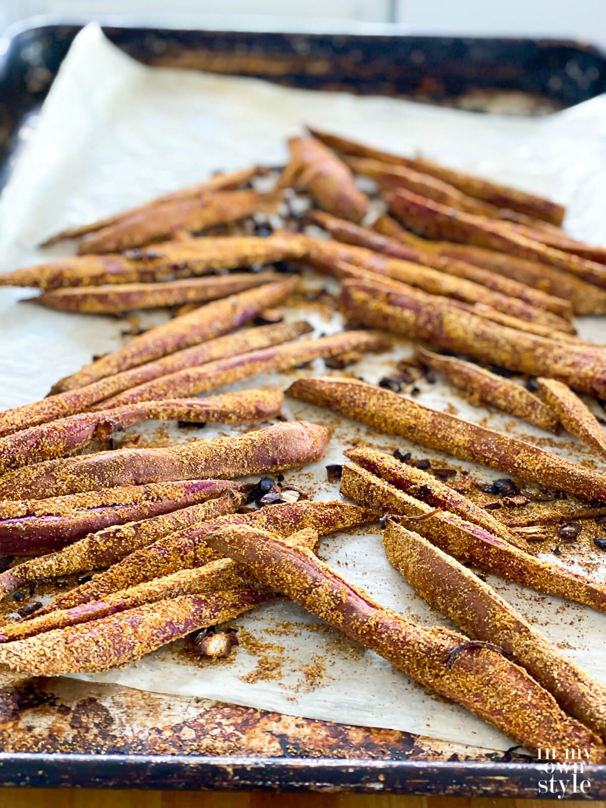 Baked purple sweet potato fries on a parchment lined baking sheet.