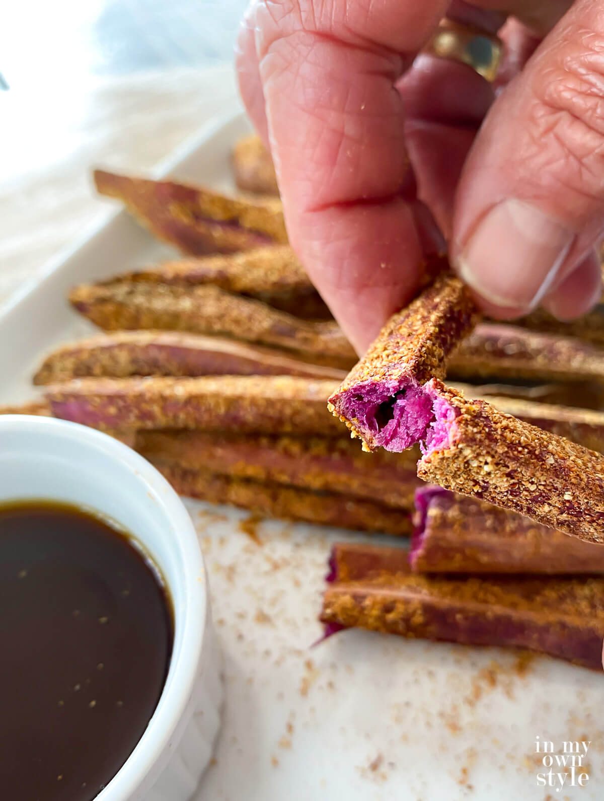 Close up of a baked sweet potato fry ready to be dipped in malt vinegar.