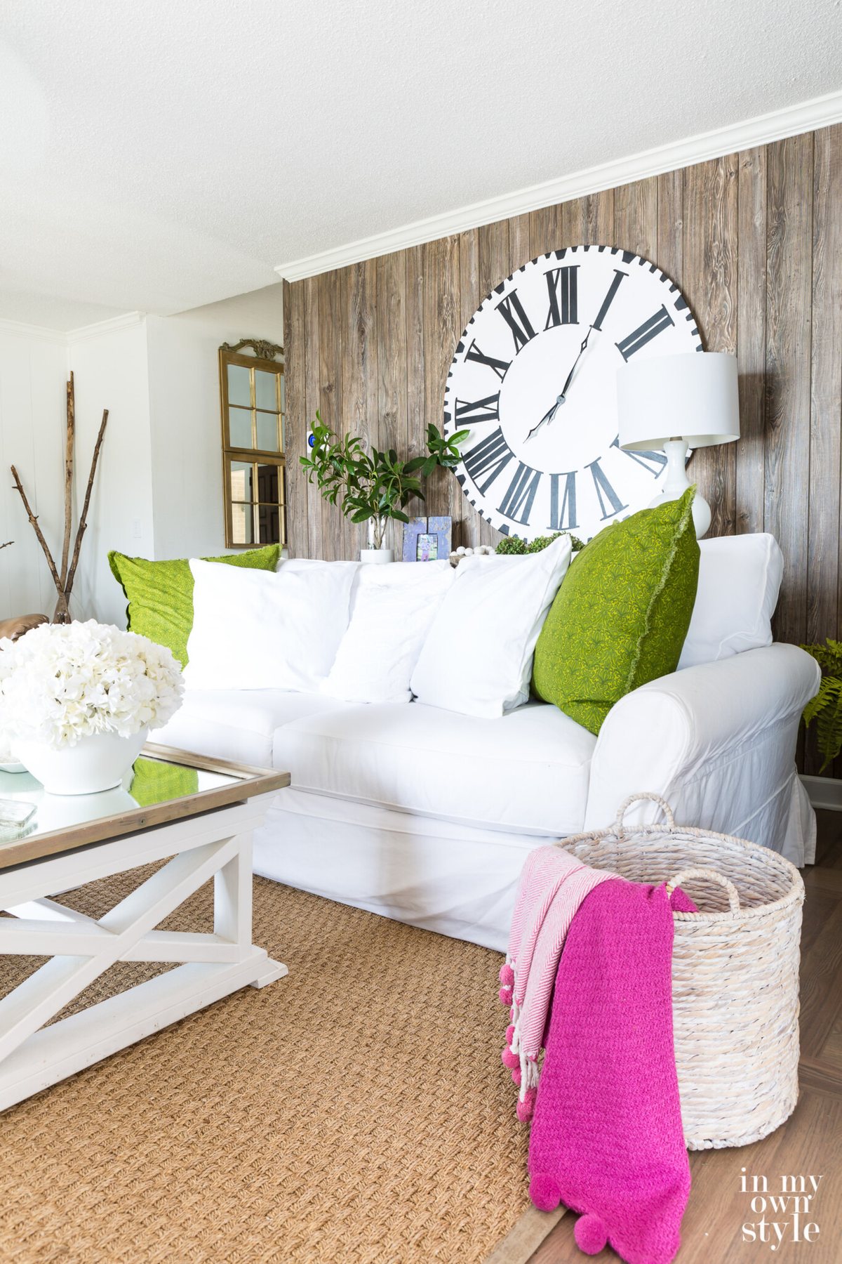 Summer decorating White sofa with green pillows in living room with faux barnwood paneling on wall.
