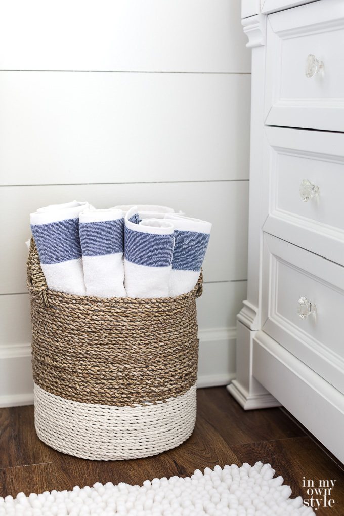 Faux-shiplap-walls painted white with white and tan wicker baskets filled with towels in front of the wall.