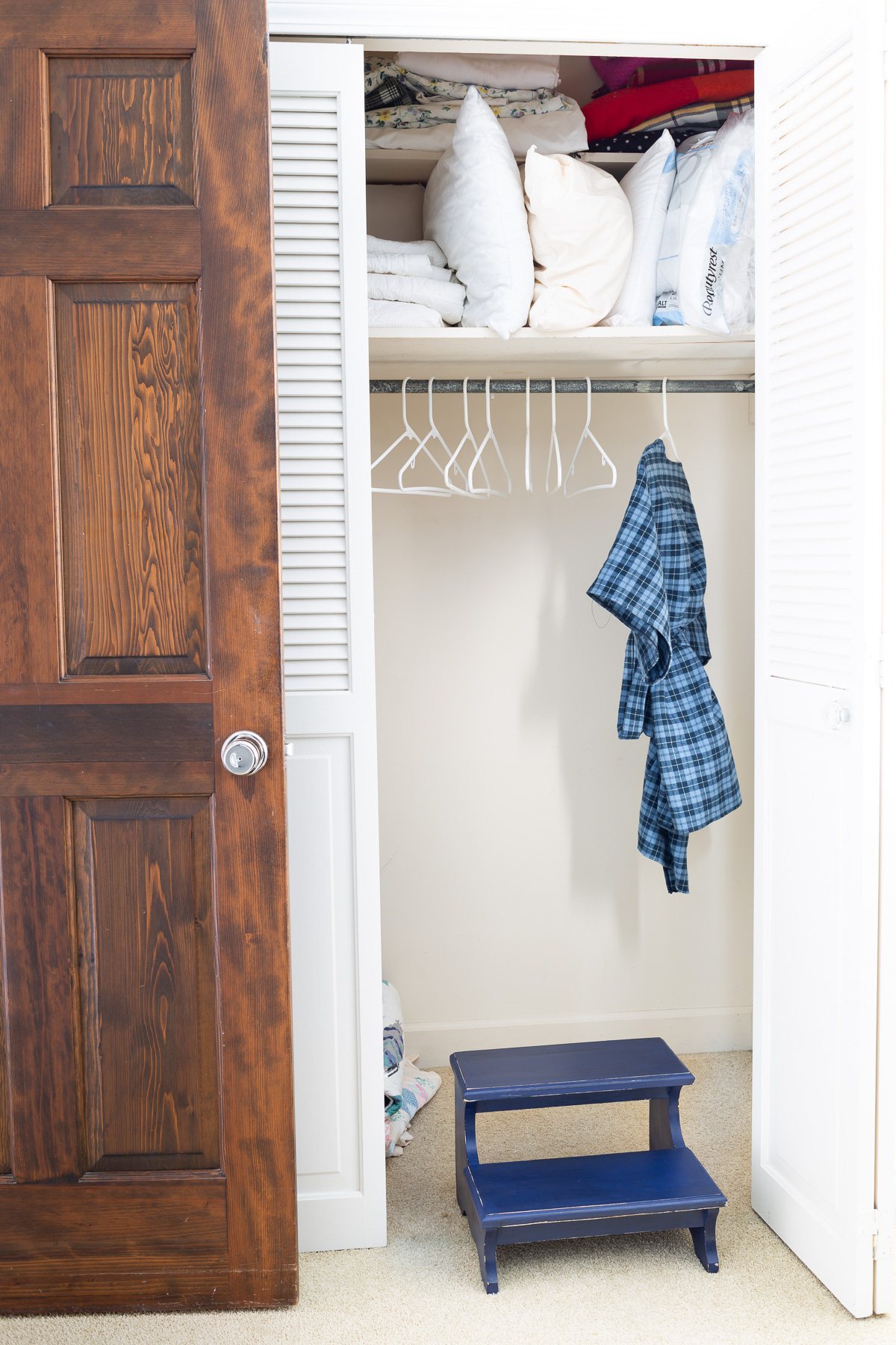 Navy blue wood step stool to stand on to get to high shelf in storage closet.