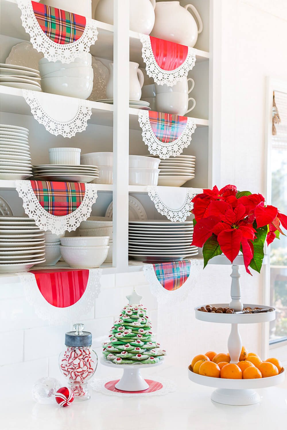White kitchen with open shelves. Red plaid doilies hanging from the shelves.
