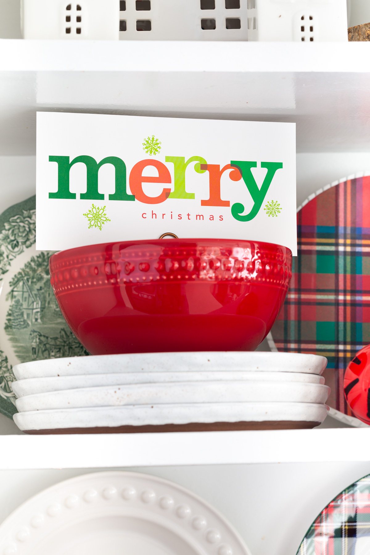 Christmas card in red bowl on open shelf that says merry.