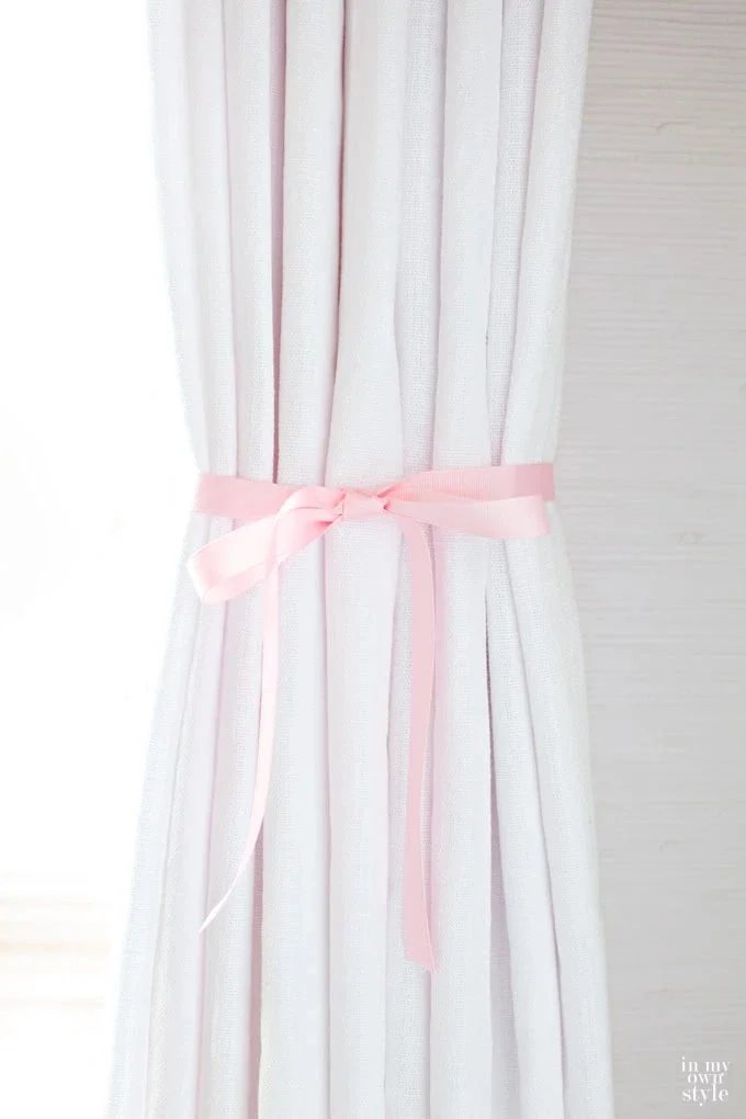 white drape hanging with pink ribbon tied around it to create pleats