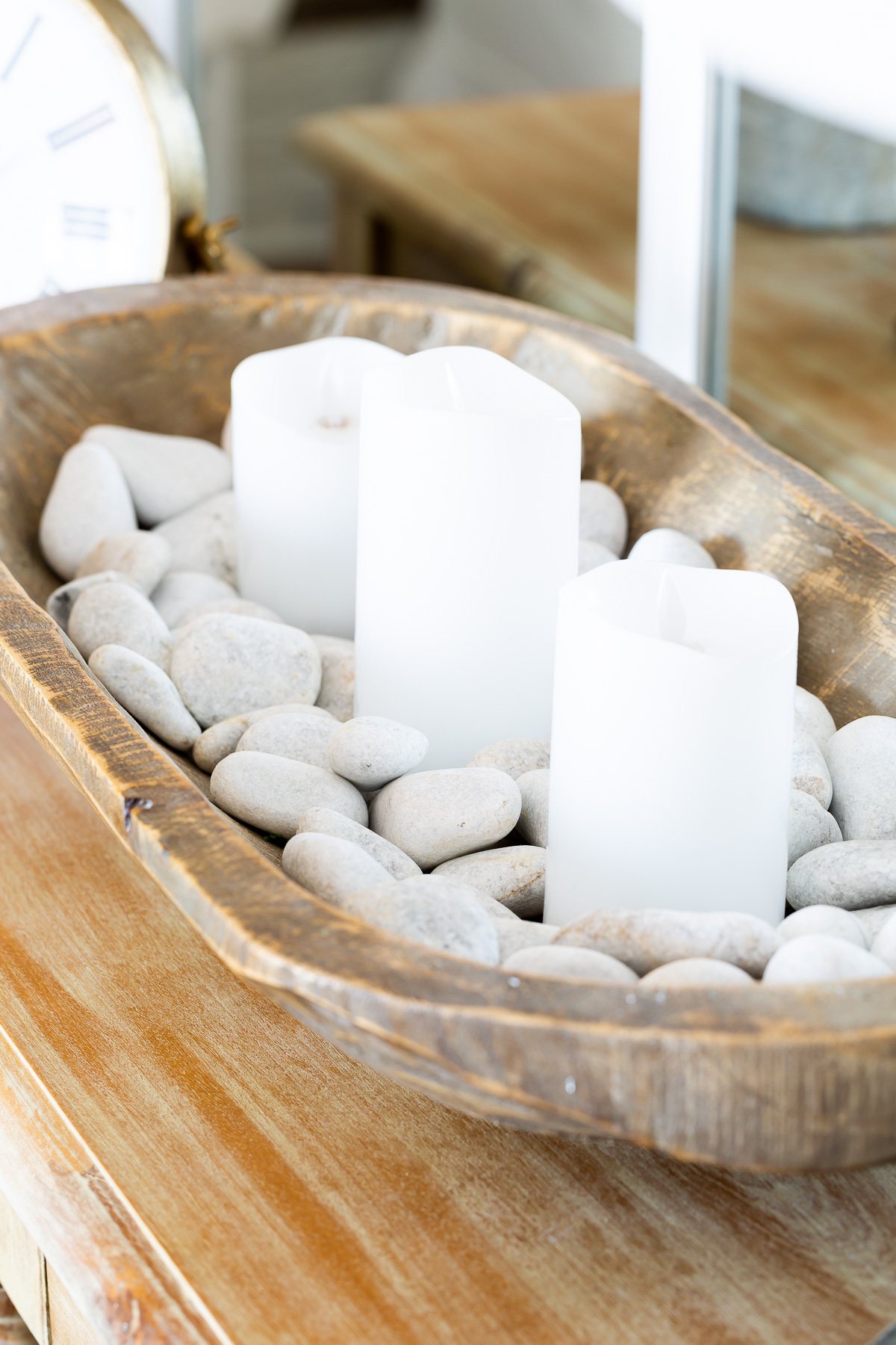 white candles in a dough bowl filled with white rocks on living room table