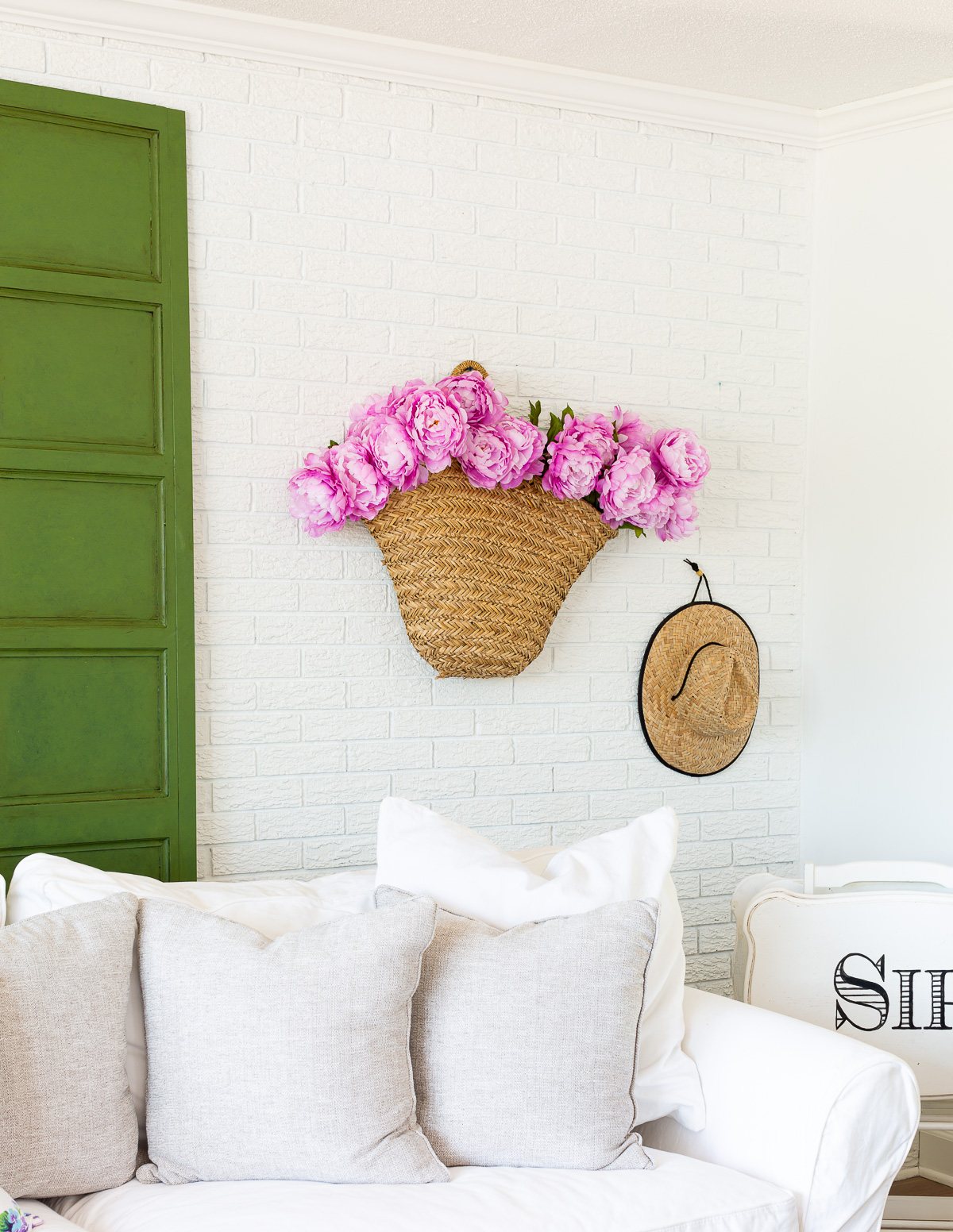 Pink peonies in a woven tote hanging on a wall.