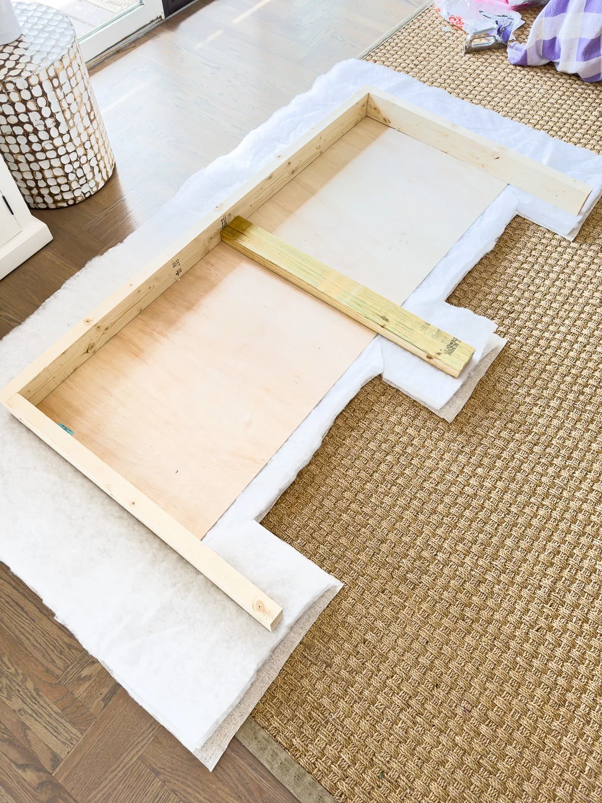 Lay fabric and batting on floor or worktable to cut them to wrap around a wood headboard frame.