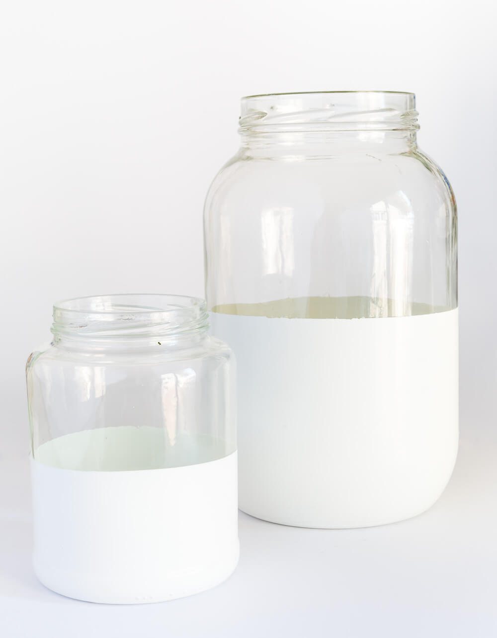 Two glass pickle jars after getting dipped or painted with white paint. They now look like trendy decor vases like the high end decorating catalogs sell.