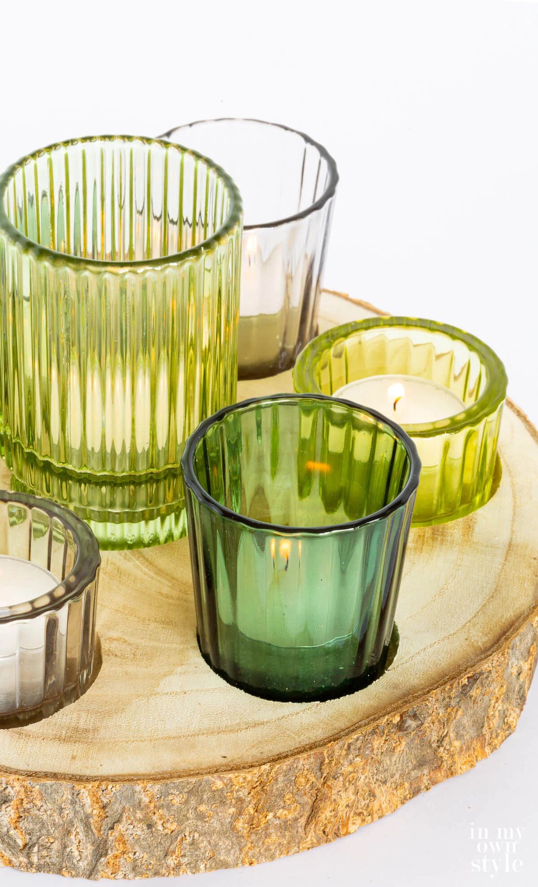 Close up of green glass candle votives in a rustic wood slice.