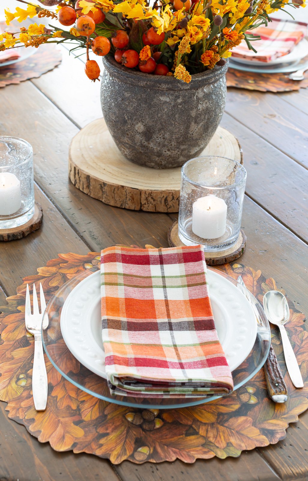 Thanksgiving table setting with a Hester & Cook fall leaves paper placemat and plaid napkin on glass plate.