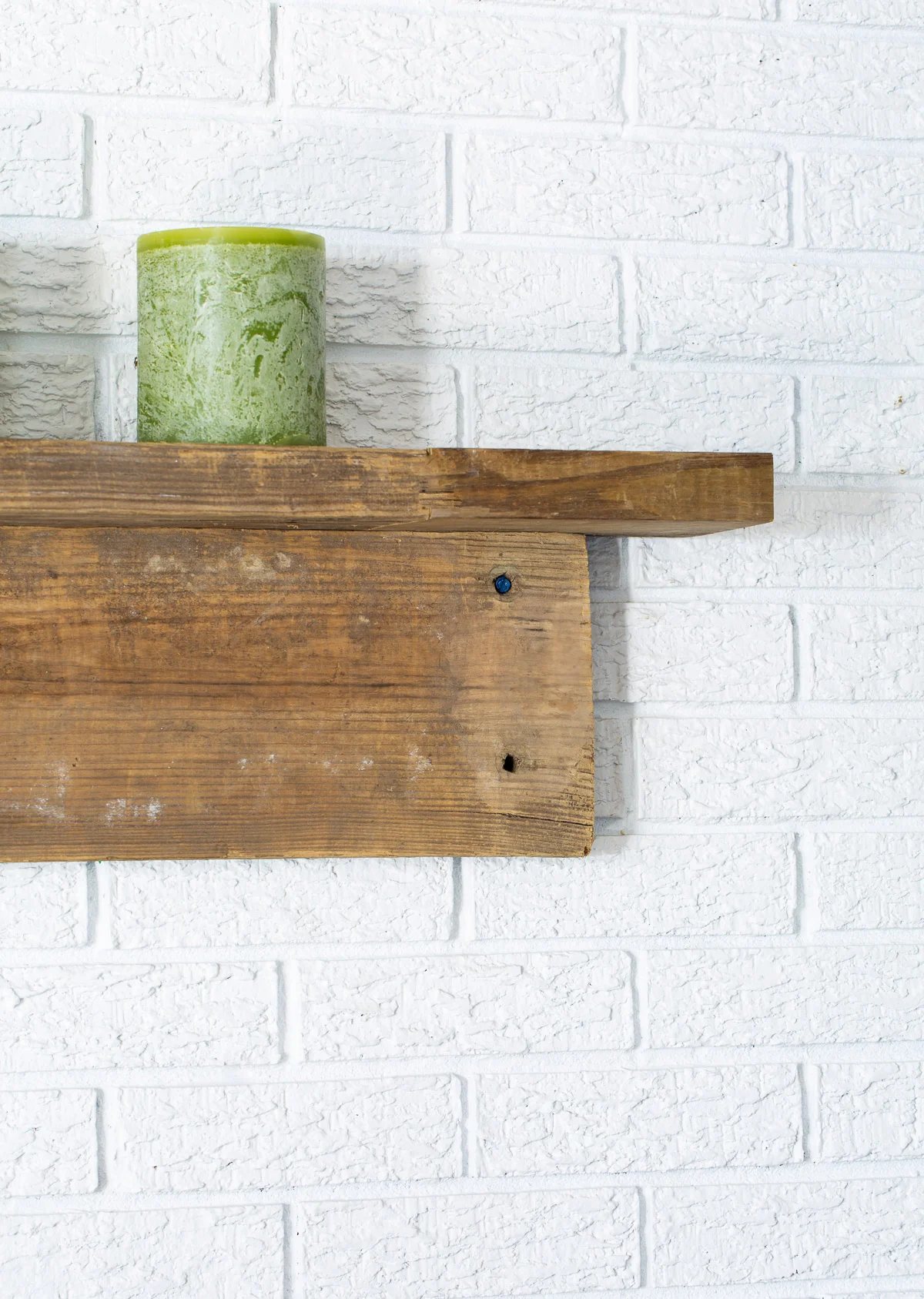 Close up of end of rustic reclaimed wood mantel on white brick wall.