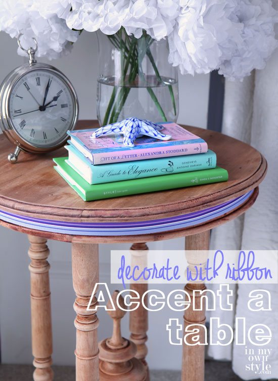 Round wood table with books and clock on the top. Purple striped ribbon is around the outer edge of the table.