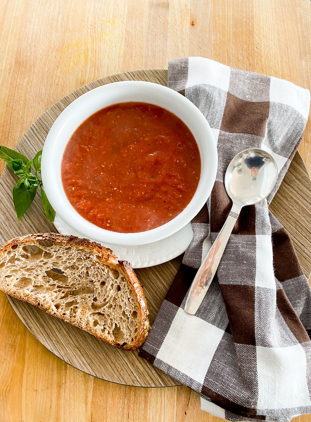 A tray with a lunch of vegan tomato soup, crusty bread a napkin and spoon.