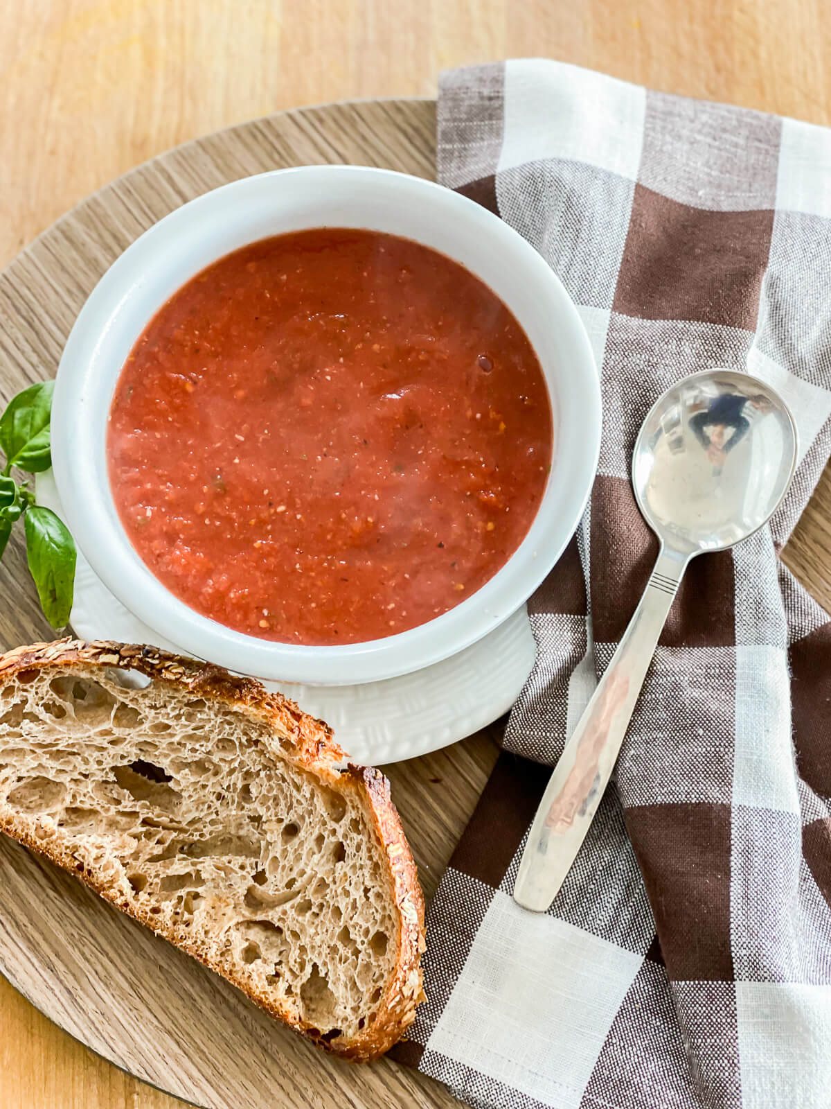A tray with a lunch of vegan tomato soup, crusty bread a napkin and spoon.