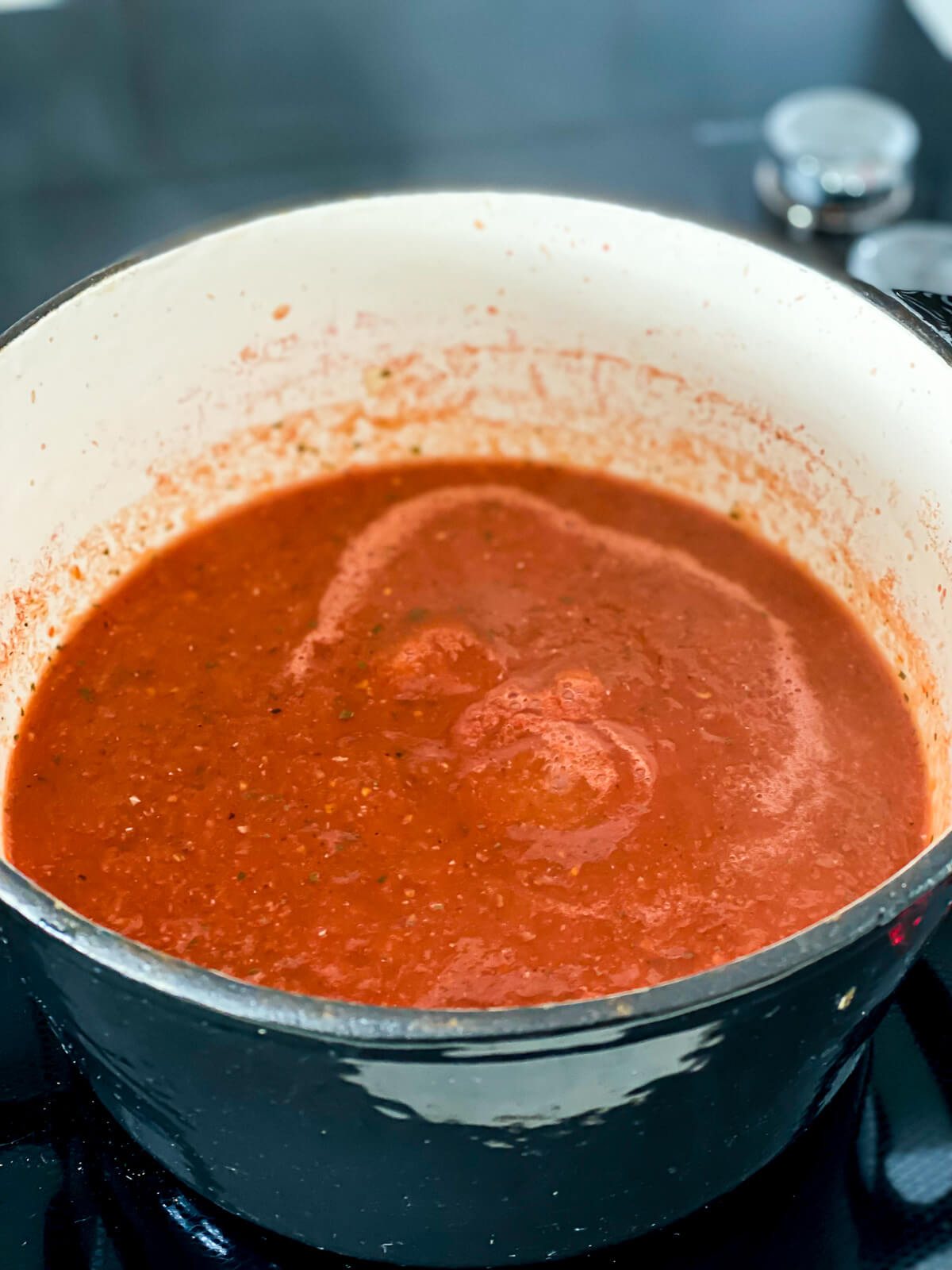 A pot of fire roasted vegan tomato soup on the stove after being blended with and immersion blender.