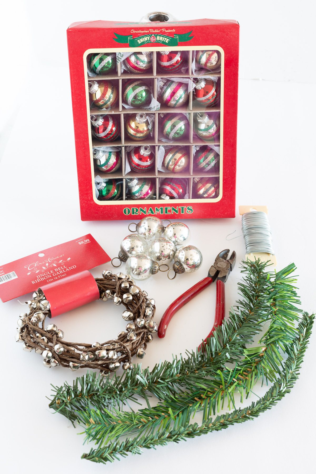 materials needed to make Christmas candle rings DIY. Mini Shiny Brite ornaments, garland ties, jingle bells and a wire cutter.