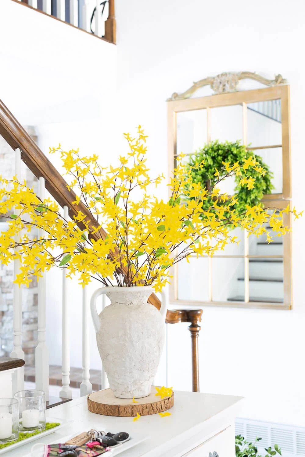 Spring forsythia blooming in vase on a foyer table. Gold mirror in the background with green wreath on it.