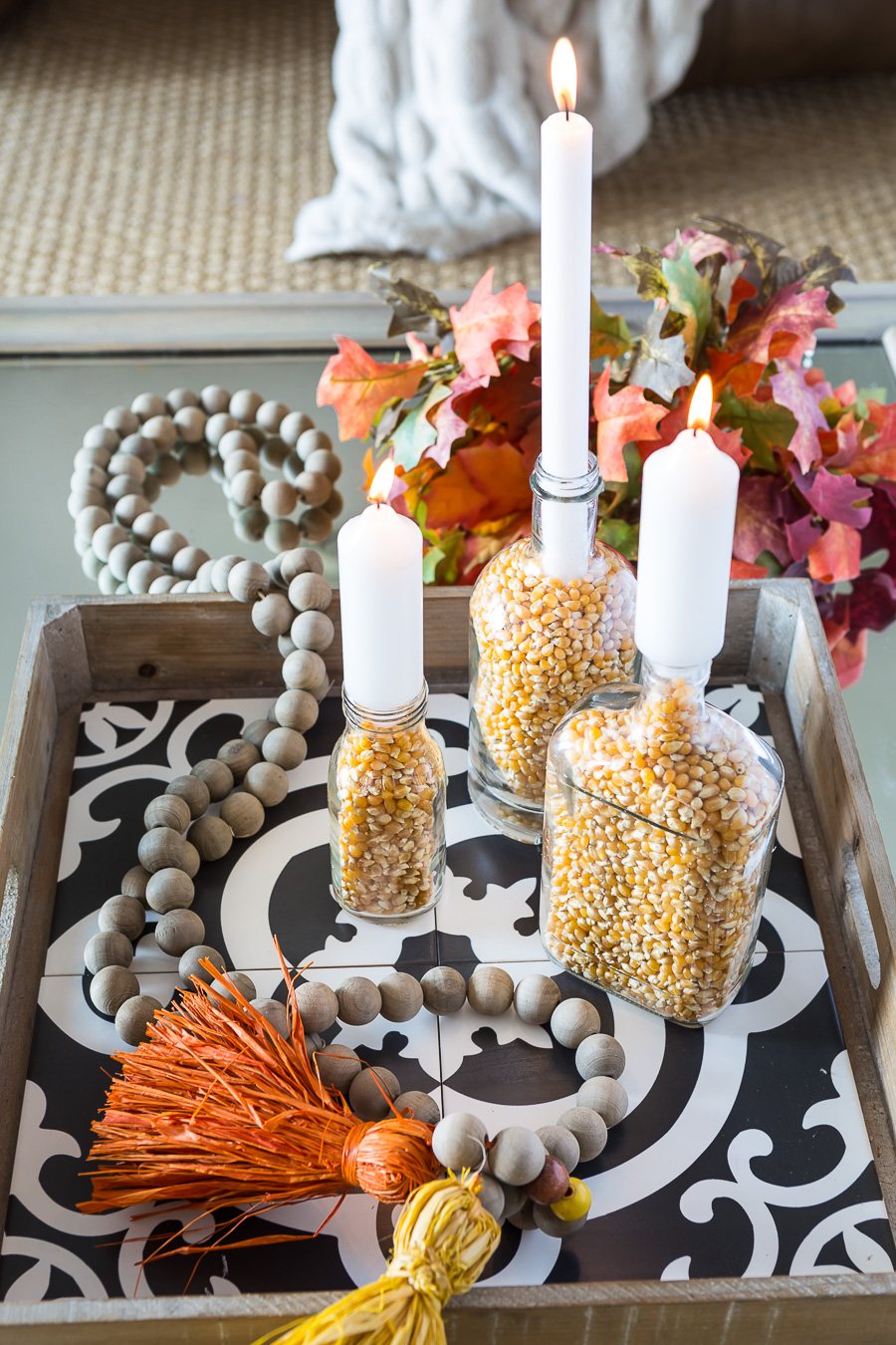 3 popcorn filled clear glass bottles on a table made into autumn inspired candle holders. Creative Fall home decorating.