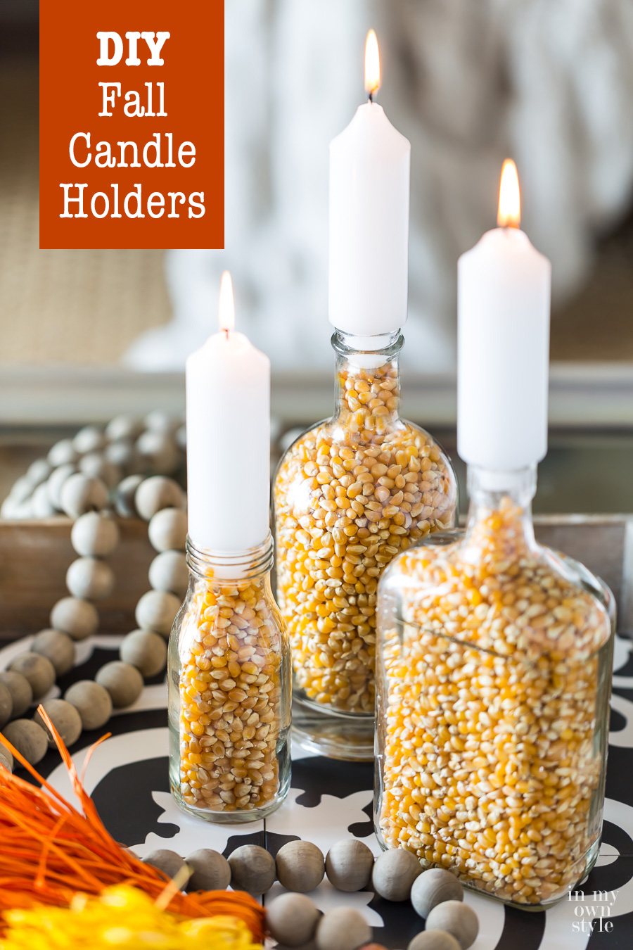 3 DIY Fall candle holders made with bottles and popcorn on a coffee table.