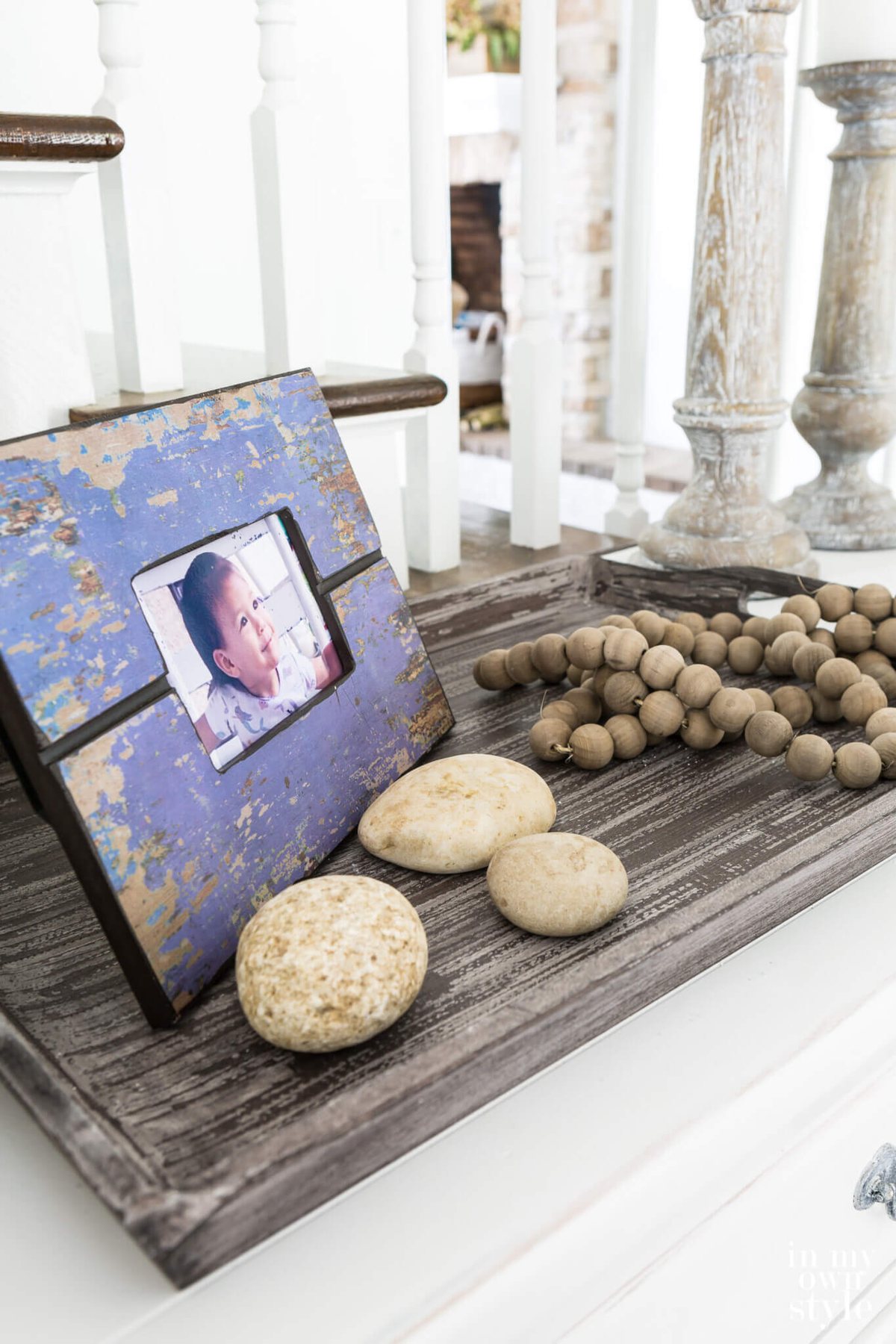 Purple distressed photo frame on tray with rocks and a wood bean garland.