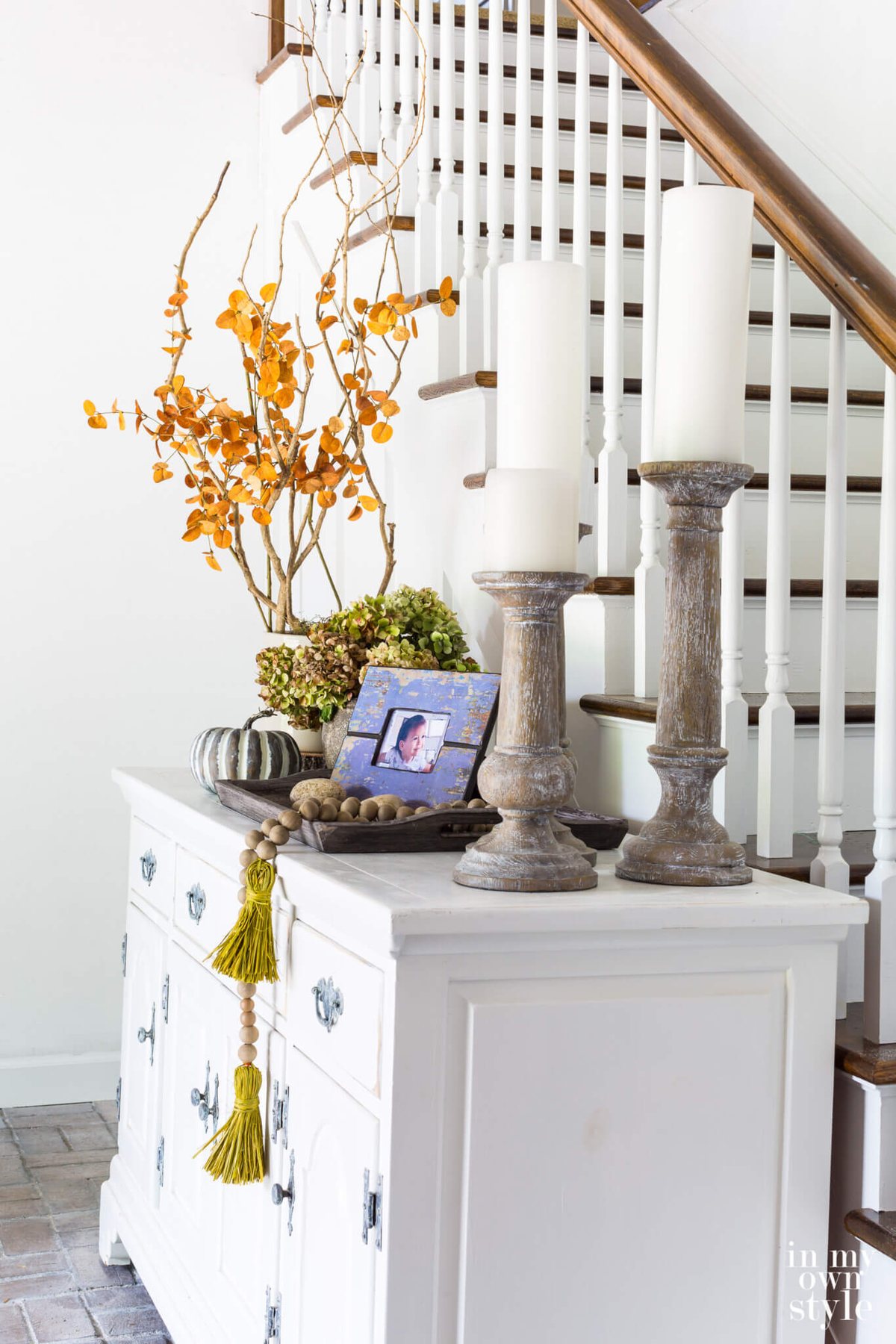 Sideboard in entryway of house decorated for fall using various heights of decor.