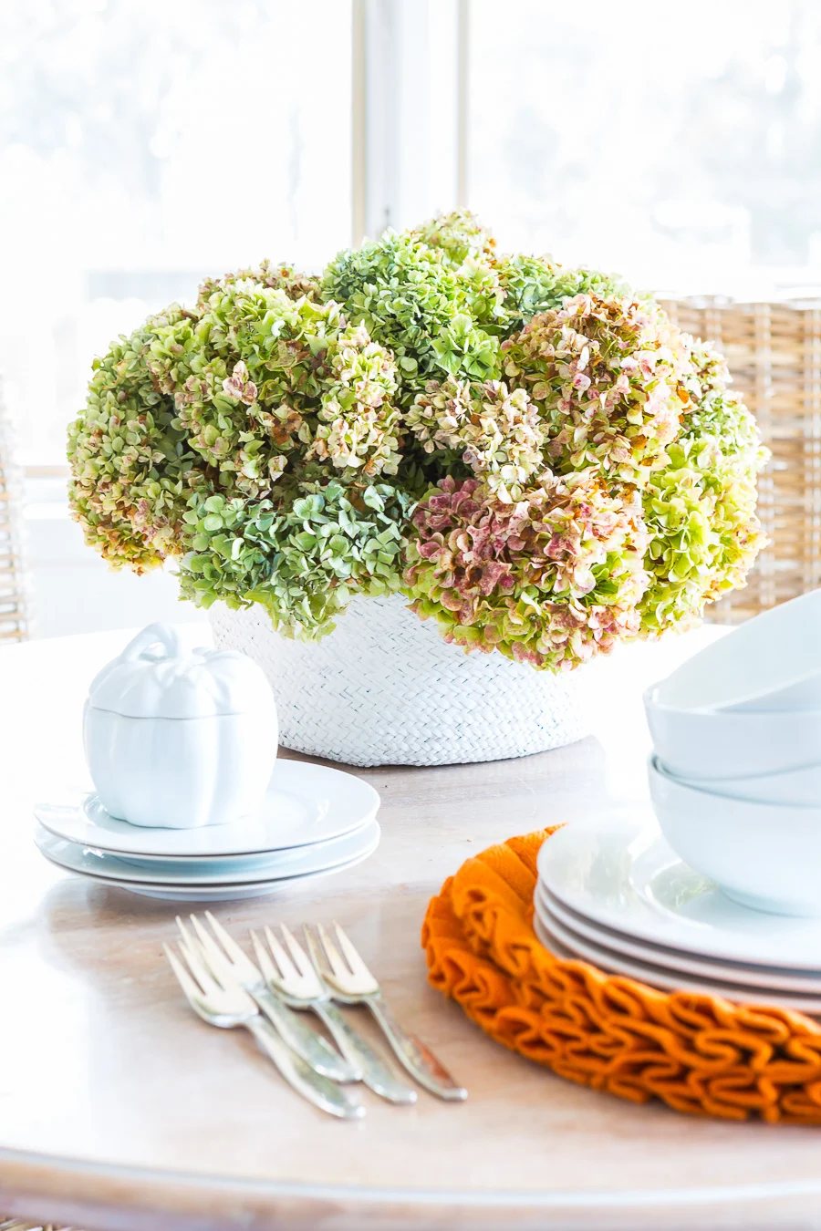Fall decorating idea using a collapsible rattan tote on a table used as a vase for dried hydrangeas.