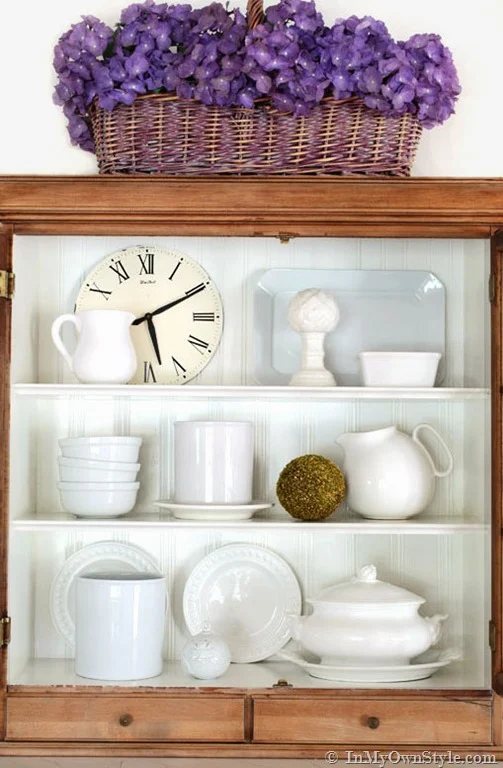 White dishes and Roman numeral clock in cabinet
