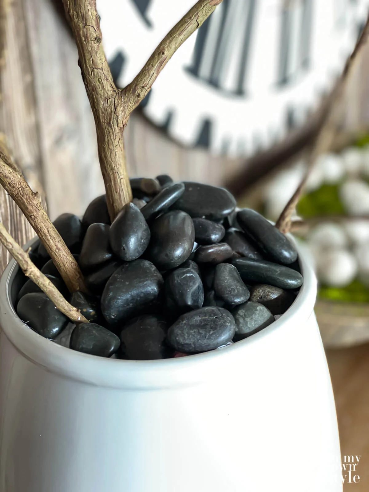 Black river rocks used instead of moss in a ceramic planter filled with Faux blooming branches.