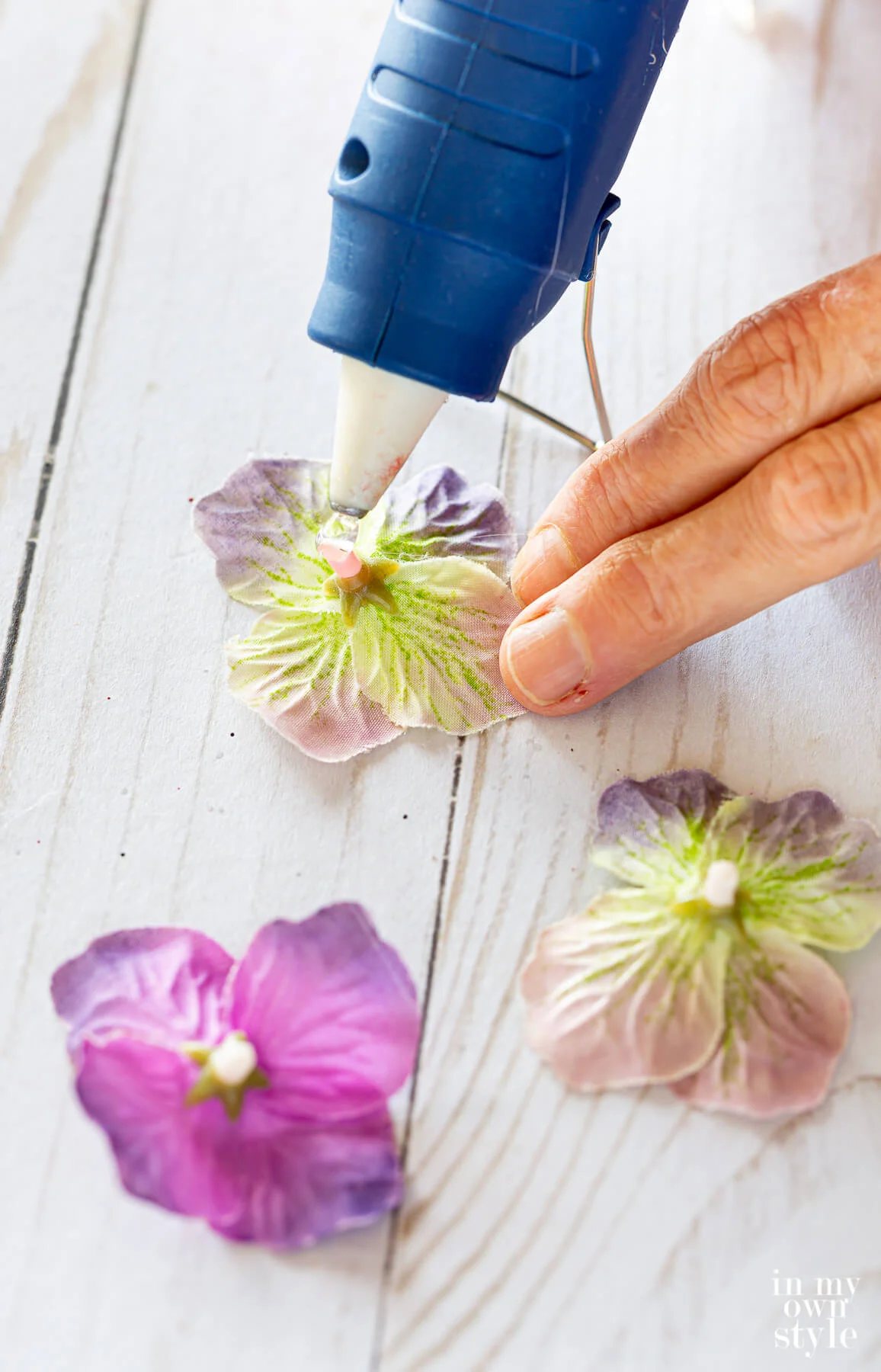Adding hot glue to the back of snipped purple flower blooms from a fake flower stem.