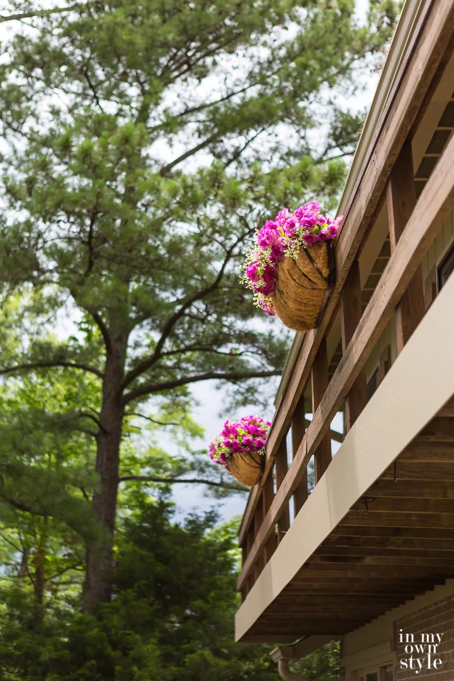 Two window flower box planters hung from deck railing on house.