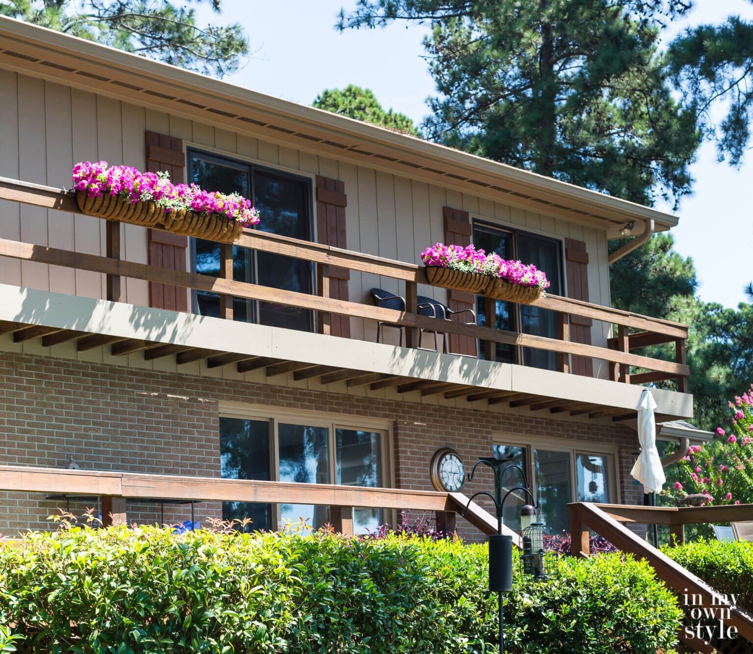 Fake pink flowers in deck railing planters on house.