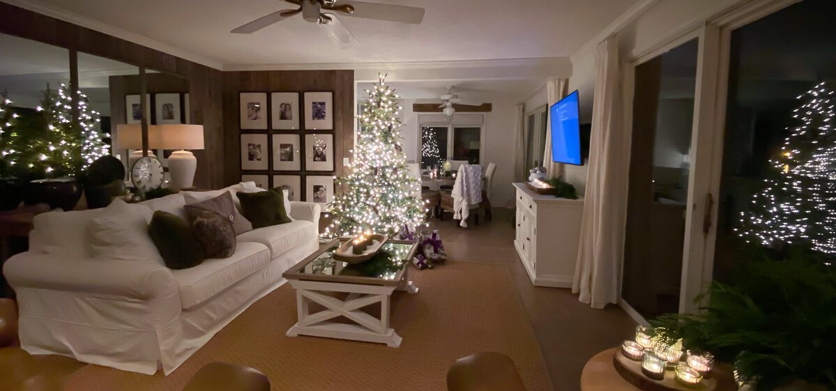 Wide angle shot at night of living room that looks like there are 4 Christmas trees in reflections.