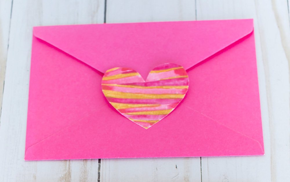 Valentine heart paper cutout glued to the flap of a pink envelope.