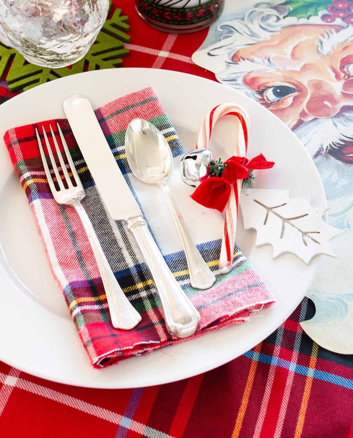 Christmas table setting ideas red and white with plaid and Santa accents. Candy cane and jingle bell on plate for decoration.