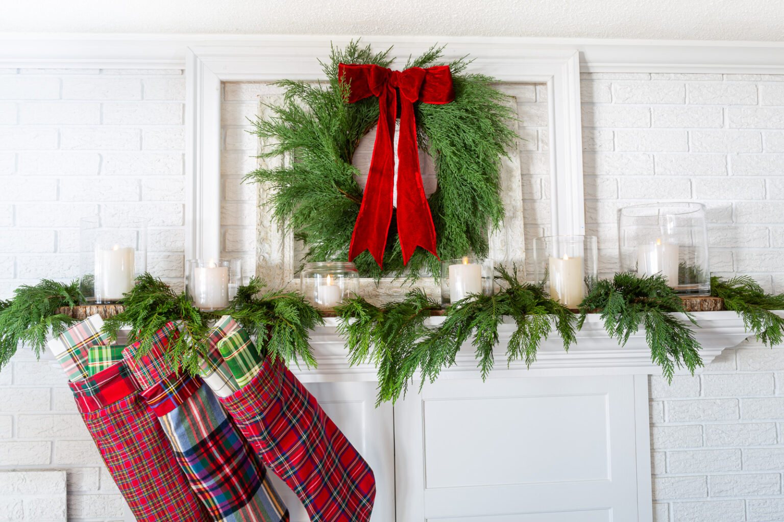 White fireplace mantel decorated for Christmas in a red, green and plaid color scheme.