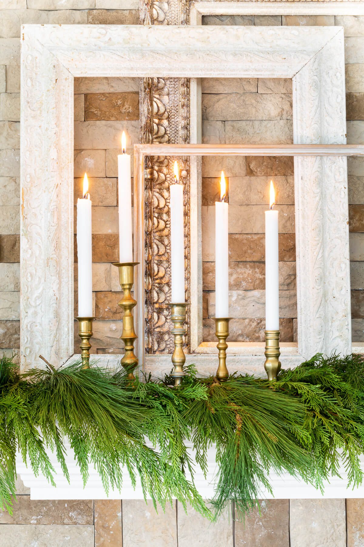 A group of brass candlesticks and white candles on mantel decorated for Christmas