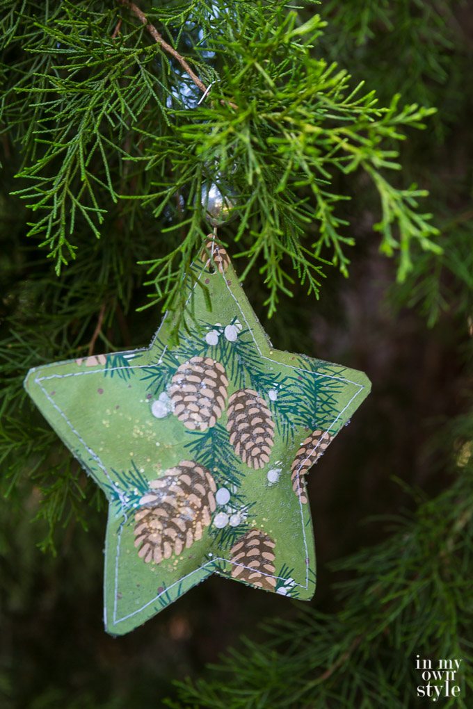 Scrapbook paper star ornament with silver bead hanging from Christmas tree.